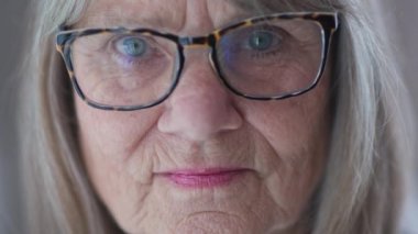 Kameraya bakan, gözlüklü, ciddi derecede kıdemli, beyaz bir kadını yakından çek. ECU 'dan emekli yaşlı beyaz kadın pencerenin önünde. Yavaş çekim 4k