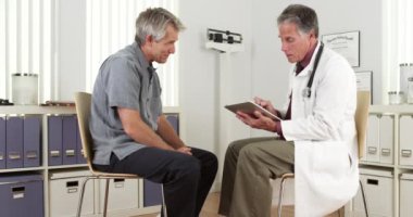 Kıdemli doktor olgun bir hastaya tabletle danışmanlık yapıyor.