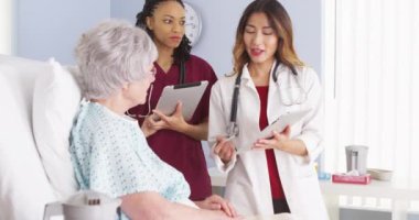 Asyalı doktor ve Afrikalı Amerikalı hemşire olgun kadın hastalarla konuşuyor.
