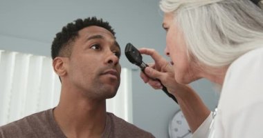 Genç siyah erkek hasta, yaşlı kadın doktor tarafından kontrol ediliyor. Afro-Amerikalı hastaların gözlerini incelemek için göz falı kullanan olgun bir kadın doktor.