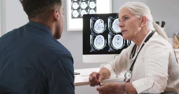 女性资深医生在脑震荡后向病人解释Ct检查的特写 与老年医生谈论他办公室里脑部X光照片的黑人病人的画像 — 图库视频影像
