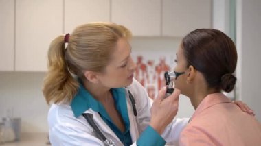 Kadın doktor hastanın kulağına bakıyor.