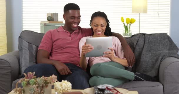 愉快的年轻黑人夫妇笑了并且使用平板电脑在沙发上 — 图库视频影像