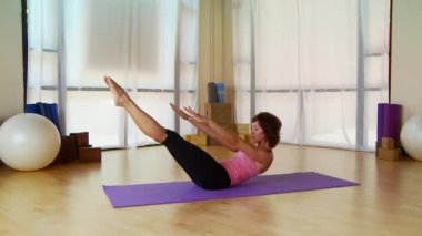 Genç bir kadın paspasın üzerinde pilate hareketi yapıyor.