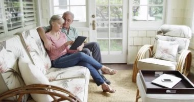 Olgun çift evdeki kanepede tablet kullanarak rahatlıyor.