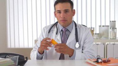 İspanyol doktor elinde ilaç şişesi tutuyor ve dinliyor.
