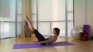 Genç bir kadın paspasın üzerinde pilate hareketi yapıyor.