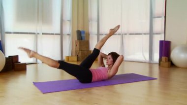 Genç bir kadın paspasın üzerinde pilate hareketi yapıyor.