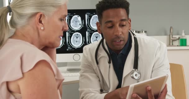 年轻的非洲裔美国医生用平板电脑向老年患者展示她的测试结果 医生和病人在室内医疗室看电子垫子的画像 — 图库视频影像