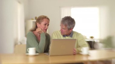 Masasında dizüstü bilgisayarlarıyla oturan sevimli yaşlı çift.