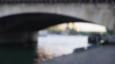Fransa 'daki Pont dIena köprüsünün arka planında bulanık bir plaka var. Seine nehrinin yanındaki çimento geçidini göremiyoruz.