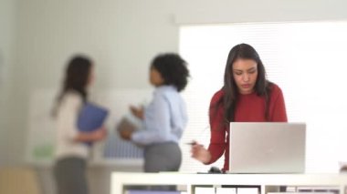 Laptop 'ta arka planda iş arkadaşlarıyla çalışan İspanyol iş kadını.