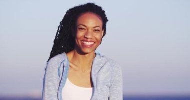 Kumsalda kameraya gülümseyen siyah kadın.