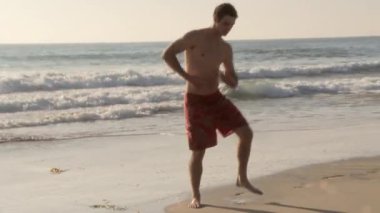 Genç adam kumsalda şapşal gibi dans ediyor.