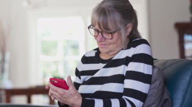 Üst düzey beyaz kadın akıllı telefondan e-posta yazıyor. Yaşlı beyaz kadın evde cep telefonuyla mesaj atıyor. Yavaş çekim el bilgisayarı 4k
