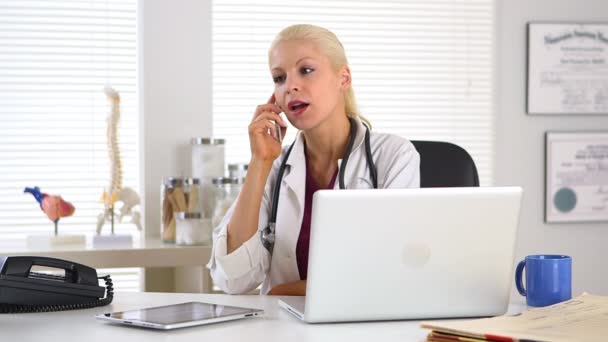 Ärztin Arbeitet Laptop Während Sie Mit Dem Handy Spricht — Stockvideo