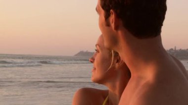 Gün batımında sahilde öpüşen genç çiftin yakın çekimi.