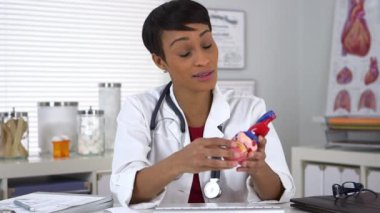 Siyah kadın doktor, kalp modelini kameraya açıklıyor.