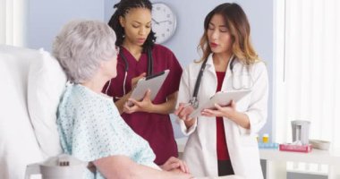 Japon Doktor ve siyah hemşire hastane yatağında yaşlı hasta ile konuşma