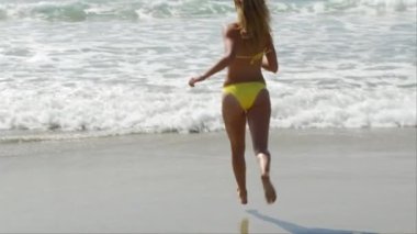 Sarı bikinili kadın okyanusa doğru koşuyor.