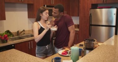 Afro-Amerikalı ve Kafkasyalı çift kahvaltıda mısır gevreği yiyor ve mutfakta konuşuyorlar. Apartmanda genç milenyumlar güne hazırlanıyor. 4k ağır çekim el bilgisayarı