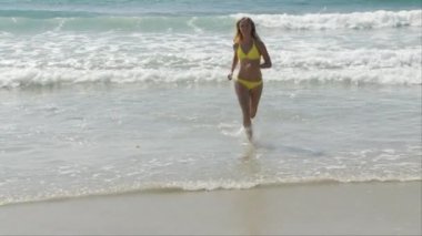 Sarı bikinili kadın okyanusta sudan çıkıyor.