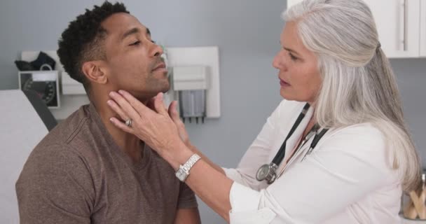 男性患者の首を調べる先輩女性医師のクローズアップ 健康診療所で医師検診を受ける魅力的な黒人男性の肖像 — ストック動画