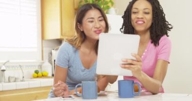 Asyalı ve Afrikalı Amerikalı arkadaşlar kahvaltı yaparken tablet bilgisayara bakıyorlar