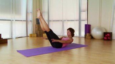 Genç bir kadın paspasın üzerinde pilate hareketi yapıyor.