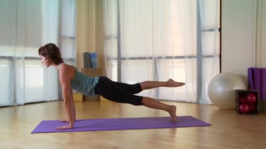 Genç bir kadın paspasın üzerinde pilate hareketi yapıyor.