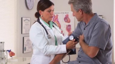 Kadın doktor yaşlı adamın tansiyonunu ölçüyor.