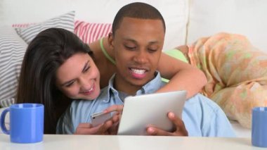 Mutlu Afro-Amerikalı ve Kafkasyalı çift tablet bilgisayar ve akıllı telefon kullanıyor.