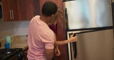 Afro-Amerikalı bir adam kız arkadaşına gizlice yaklaşırken o da buzdolabına bakıyordu. Mutfaktaki beyaz kadın erkek arkadaşı tarafından şaşırtıldı. 4k ağır çekim el bilgisayarı