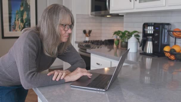 在厨房用手提电脑从家里上网工作的高级白人妇女的手持照片 中镜头的老年白人女士工作在柜台上的Pc 慢动作4K — 图库视频影像