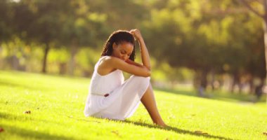 Genç siyahi kadın parkta oturmuş düşünüyor.