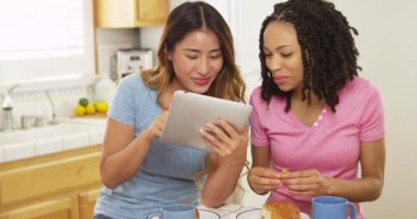 Siyah ve Asyalı arkadaşlar kahve içip tablet bilgisayar kullanıyorlar.