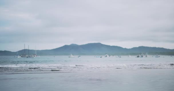 船底板在平静的海浪中滚动 热带海滩上的帆船在地平线上俯瞰群山的景象 — 图库视频影像
