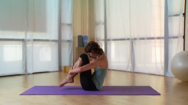 Genç bir kadın paspasın üzerinde pilate hareketi yapıyor.