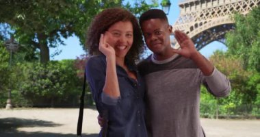 Eyfel Kulesi 'nin yanındaki Afrikalı Amerikalı çift gülümseyip kameraya el sallıyor. Siyahi erkek ve kadın Paris 'te poz veriyor. 4k