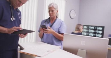 Olgun erkek ve kadın tıp uzmanları tablet bilgisayar ve cep telefonuna bakıyor.