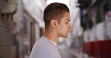 Kentin arka sokağında duran havalı kesimli İspanyol adamın yan görüntüsü. Latino Millennial 'ın yakın plan portresi. 4k