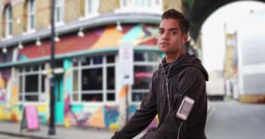 Londra 'nın hippi mahallesindeki Latin koşucunun portresi sokaklarda koşuya ara veriyor. Akıllı telefondan müzik dinleyen ve doğrudan kameraya bakan zinde İspanyol bir koşucu. 4k