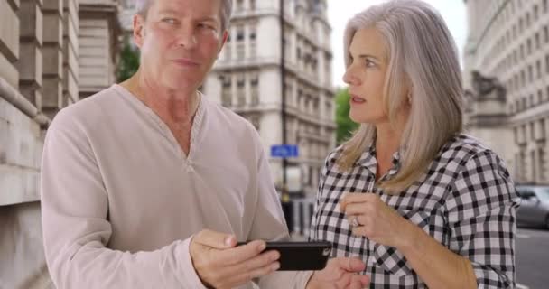 ロンドンを旅行する白人の老夫婦は方向性について議論する 夫と妻はどこへ行くべきかわからないスマートフォンを見てロンドンで迷子になりました — ストック動画