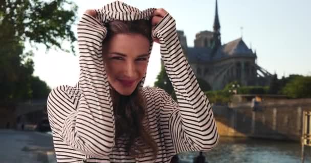 フランス旅行中の若い女性がパリで喜んでポーズをとっています パリの白人のミレニアル世代の観光客は ノートルダムを背景にカメラを笑っています — ストック動画