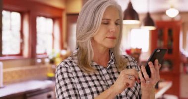 Orta yaşlı, beyaz bir kadının cep telefonuyla çekilmiş bir fotoğrafı var. Akıllı telefonla mesaj okuyan hoş, son sınıf öğrencisi bir kadın..