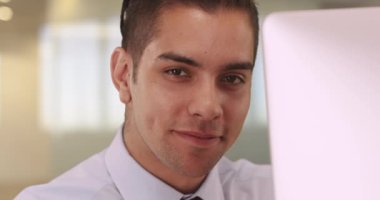 Bilgisayarda oturmuş gülümseyen yakışıklı Latin iş adamının portresi. Ofiste kameraya bakan çekici, mutlu, genç bir İspanyol profesyonel. 4k