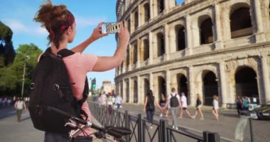 Bisikletli kadın İtalya, Roma 'da iken Colosseum' un bir videosunu çekmek için duruyor. Roma 'da bisiklet süren beyaz kadın turist Colosseum' un videosunu çekiyor. 4k