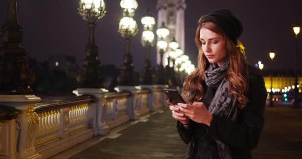在法国巴黎的亚历山大港3号上 一个漂亮的黑发姑娘用她的智能手机旅行 年轻的白人美女在巴黎度假 晚上发短信给她的朋友 — 图库视频影像