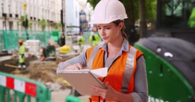 Yoğun bir inşaat alanındaki bazı belgelere bakan kendine güvenen genç bir kadın müteahhit. Ekibini denetleyen bir şantiyede çalışan beyaz bir kadın. 4k