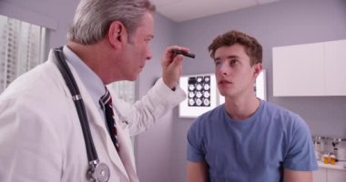 Orta yaşlı doktor genç yetişkin erkek hasta gözünde incelenmesi